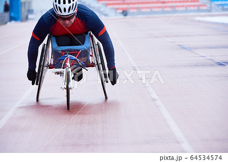 Determined athlete in sportswear and helmet participating in wheelchair race Determined athlete in sportswear and helmet participating in wheelchair race 64534574