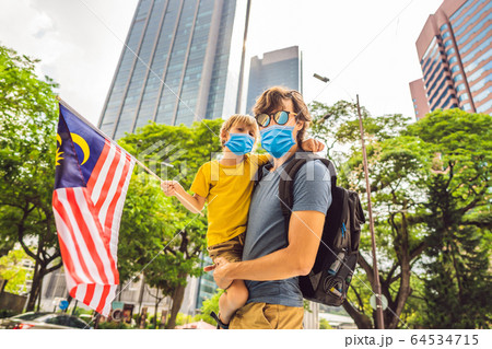 Dad and son in medical mask tourists in Malaysia with the flag of Malaysia near the skyscrapers Dad and son in medical mask tourists in Malaysia with the flag of Malaysia near the skyscrapers 64534715