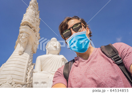 Man tourist in medical mask on background of Big Buddha statue Was built on a high hilltop of Phuket Man tourist in medical mask on background of Big Buddha statue Was built on a high hilltop of Phuket 64534855