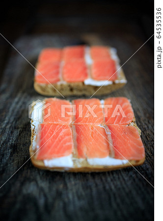 Two whole grain bread toasts with cream cheese and lightly salted salmon on a dark wooden board 64535536