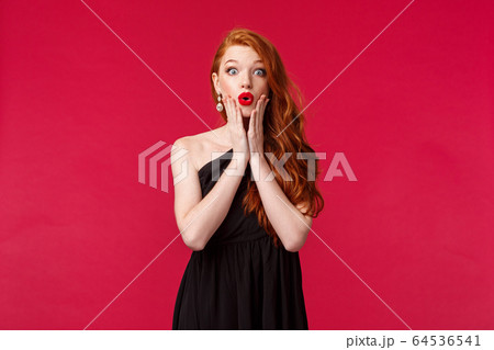 Fashion, luxury and beauty concept. Amused and interested, surprised elegant young woman in black luxurious dress, touch face folding lips amazed, gossiping at party, red background 64536541