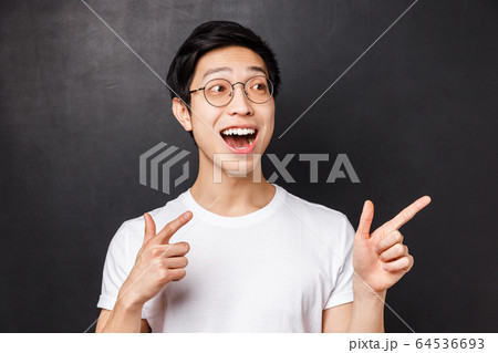 Close-up portrait of excited and happy, cheerful asian guy looking at something incredibly awesome, pointing and staring right side, smiling astounded and fascinated, black background Close-up portrait of excited and happy, cheerful asian guy looking at something incredibly awesome, pointing and staring right side, smiling astounded and fascinated, black background 64536693