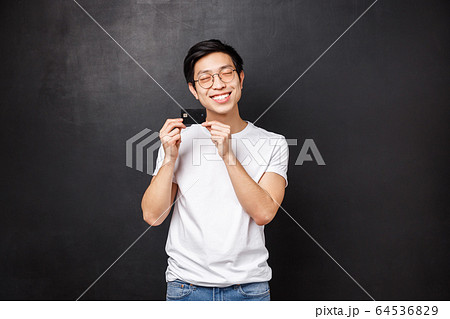 Bank, finance and payment concept. Portrait of silly and happy asian man in t-shirt, close eyes satisfied introducing his first credit card, ready go shopping and waste some money, black background Bank, finance and payment concept. Portrait of silly and happy asian man in t-shirt, close eyes satisfied introducing his first credit card, ready go shopping and waste some money, black background 64536829