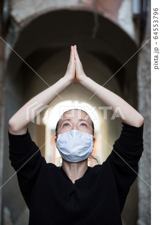 Coronavirus outbreak. Young caucasian woman wearing medical protection face mask praying over coronavirus global pandemic, for salvation of humanity, health, anxiety and depression reduction 64553796