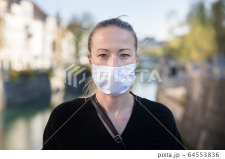 COVID-19 pandemic coronavirus. Young girl in city street wearing face mask protective for spreading of coronavirus disease 2020. Close up of young woman with medical mask on face against SARS-CoV-2 COVID-19 pandemic coronavirus. Young girl in city street wearing face mask protective for spreading of coronavirus disease 2020. Close up of young woman with medical mask on face against SARS-CoV-2 64553836