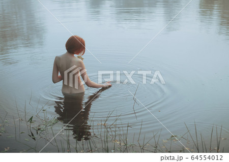 Naked woman standing to waist in cold lake 64554012
