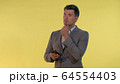 Tall man in suit holding one hand on chin, looking on smartphone and thinking about something. 64554403