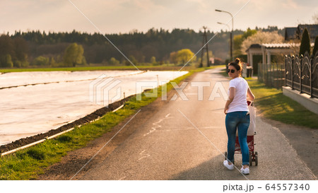 Young mother and child in the red stroller walks 64557340