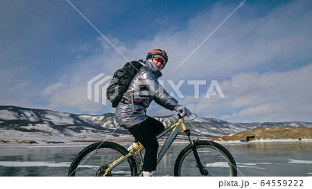 Woman is riding bicycle on the ice. Tires on bike are covered wi Woman is riding bicycle on the ice. Tires on bike are covered wi 64559222