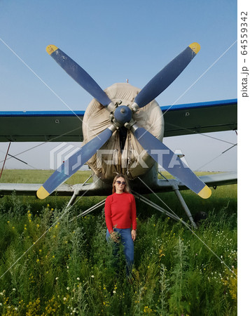 Woman portrait in front of an aircraft. Young beautiful woman with red jacket stand in front of older bomber aircraft with propeller in background. Woman portrait in front of an aircraft. Young beautiful woman with red jacket stand in front of older bomber aircraft with propeller in background. 64559342