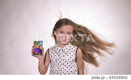 Child with headphones dancing at studio background. Girl listens to music on smartphone. Beautiful cute happy little girl listens to music. Child with headphones dancing at studio background. Girl listens to music on smartphone. Beautiful cute happy little girl listens to music. 64559902