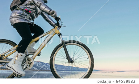 Woman is riding bicycle on the ice. Tires on bike are covered wi 64559932