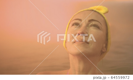 Close up caucasian woman in a swim in hot saline mineral water bath at a traditional spa outdoor with soft magic pink lighting steam. Geothermal spa. 64559972