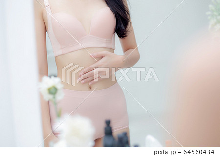 Beautiful young asian woman in underwear looking mirror applying cream and lotion on belly 64560434