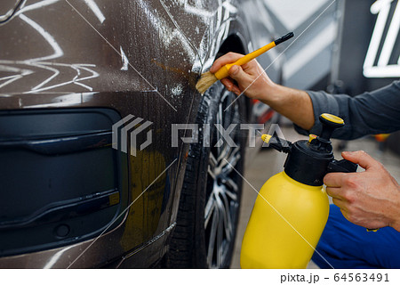 Worker cleans car with spray and brush, detailing 64563491