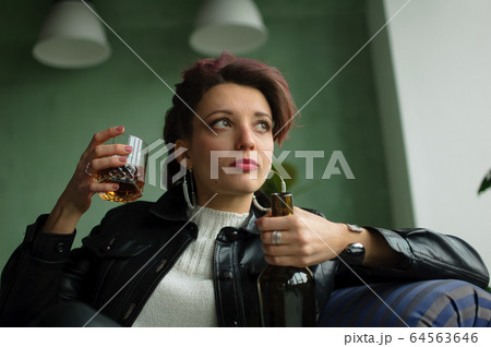 Young sad woman with dark pink hair with glam rock style look is drinking whisky from a glass with abomination grimace on the face, female alcoholism, alcohol addiction 64563646