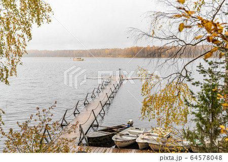 The Long pier on the lake, Terrace at the lake, the Autumn at the lake Boroye, Boats at a pier, Valday national park, Russia, panoramic image, golden trees, Wooden lodges, cloudy weather 64578048