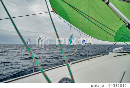 Croatia, Adriatic Sea, 19 September 2019: The race of sailboats, the team sits on the edge of a boat board, bright colors, view of participants of race from other boat through ropes and sails Croatia, Adriatic Sea, 19 September 2019: The race of sailboats, the team sits on the edge of a boat board, bright colors, view of participants of race from other boat through ropes and sails 64582012