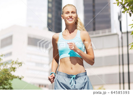 smiling young woman running at city 64585393
