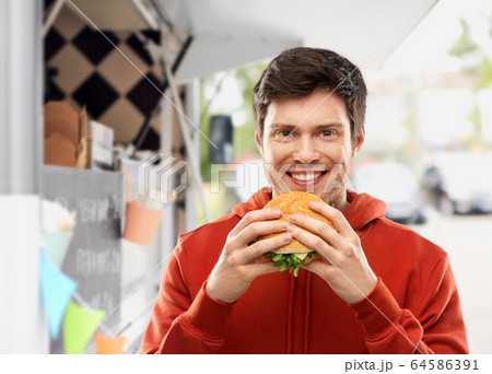 happy young man eating hamburger at food truck happy young man eating hamburger at food truck 64586391