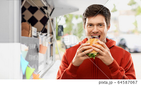 happy young man eating hamburger at food truck 64587067
