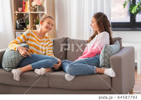 happy teenage girls talking on sofa at home happy teenage girls talking on sofa at home 64587793