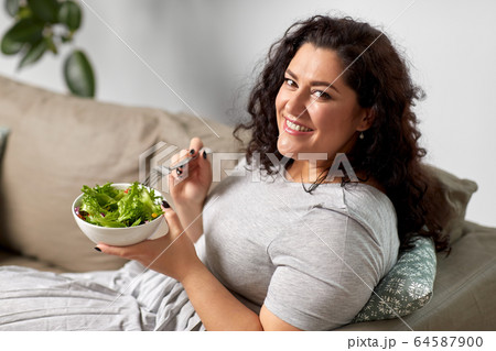 smiling young woman eating vegetable salad at home 64587900