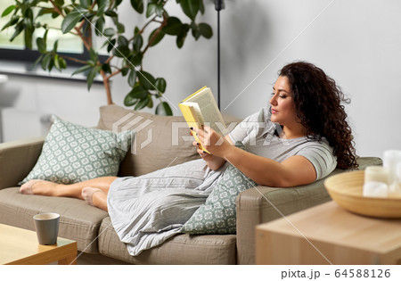 young woman reading book on sofa at home 64588126