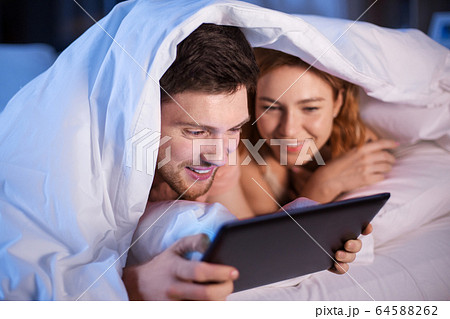 happy couple using tablet pc in bed at night happy couple using tablet pc in bed at night 64588262