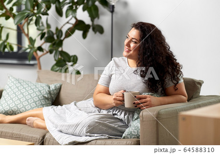 happy woman drinking coffee or tea on sofa at home 64588310
