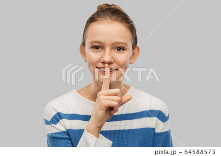 smiling teenage girl with finger on lips smiling teenage girl with finger on lips 64588573