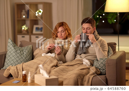 sick couple with thermometer and tea at home 64588760