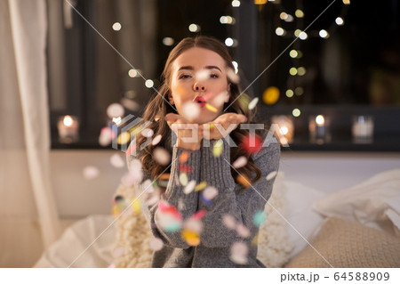 woman blowing confetti from her hands at home woman blowing confetti from her hands at home 64588909
