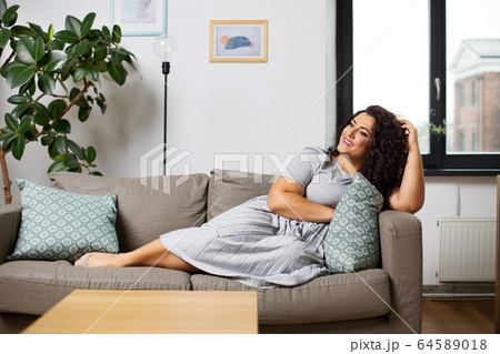 happy young woman lying on sofa at home 64589018