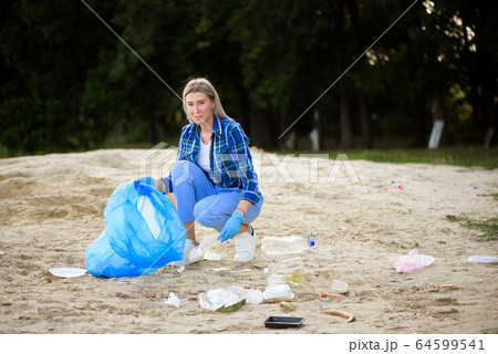Young volunteer picking up plastic bottles on the beach near the park. Young volunteer picking up plastic bottles on the beach near the park. 64599541