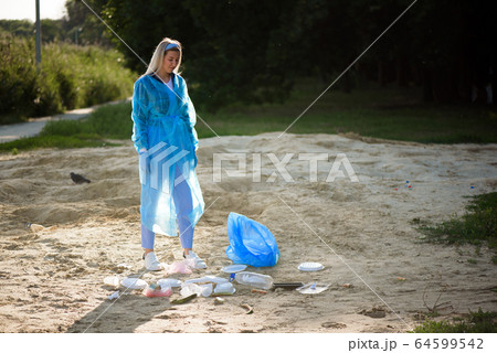 Young volunteer picking up plastic bottles on the beach near the park. 64599542