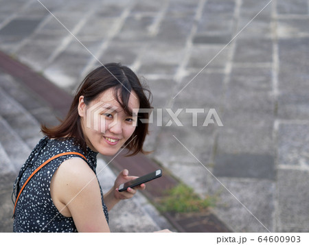 A woman smiling into the camera while holding her phone A woman smiling into the camera while holding her phone 64600903