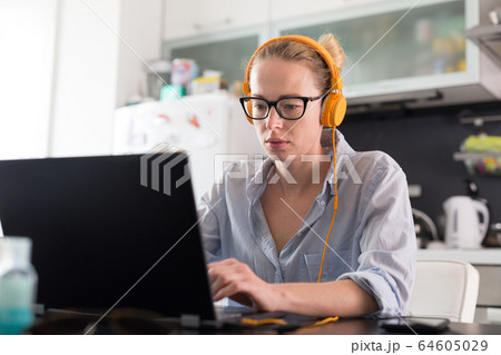 Female freelancer in her casual home clothing working remotly from her dining table in the morning. Home kitchen in the background. 64605029