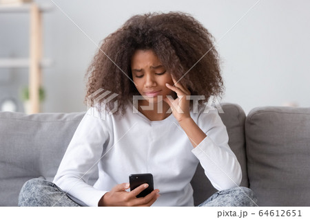 Upset depressed african teen girl looking at phone at home 64612651