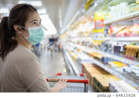 Asian woman wear a mask,looking fresh water and milk,choosing necessary food products,people panic buying and hoarding during the Covid-19,Coronavirus epidemic,girl preparing for pandemic quarantine Asian woman wear a mask,looking fresh water and milk,choosing necessary food products,people panic buying and hoarding during the Covid-19,Coronavirus epidemic,girl preparing for pandemic quarantine 64615926