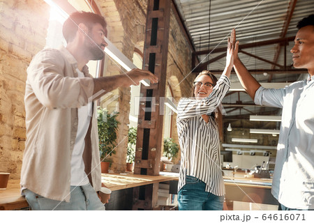 Give me five! Young man and woman giving high-five while having coffee break with colleagues in the modern office Give me five! Young man and woman giving high-five while having coffee break with colleagues in the modern office 64616071