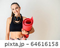 Sporty woman with headphones and rolled mat 64616158