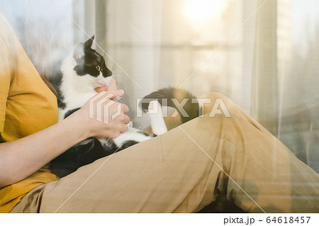 Sad girl in medical protective mask and yellow t-shirt sitting on the windowsill with a black and white Tuxedo cat during a pandemic quarantine coronavirus Covid-19. Isolation at home. Sad girl in medical protective mask and yellow t-shirt sitting on the windowsill with a black and white Tuxedo cat during a pandemic quarantine coronavirus Covid-19. Isolation at home. 64618457