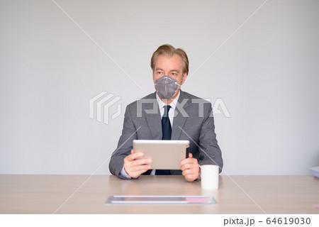Mature businessman using digital tablet with mask for protection from corona virus outbreak at work Mature businessman using digital tablet with mask for protection from corona virus outbreak at work 64619030