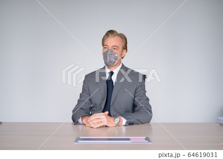 Mature businessman working with mask for protection from corona virus outbreak at work Mature businessman working with mask for protection from corona virus outbreak at work 64619031