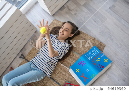 Girl lying on the floor mat with a tennis ball. 64619360