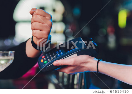 close up hand of young customer male paying with credit transaction by smart watch contactless terminal in modern shop, NFC technology. close up hand of young customer male paying with credit transaction by smart watch contactless terminal in modern shop, NFC technology. 64619410