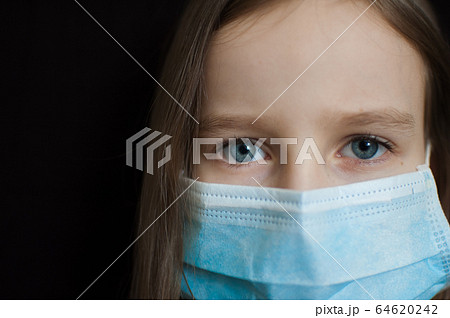 Close-up portrait of little defenseless girl on black backgound in blue disposable mask for protection of Coronavirus Covid-19 during self-isolation at home Close-up portrait of little defenseless girl on black backgound in blue disposable mask for protection of Coronavirus Covid-19 during self-isolation at home 64620242