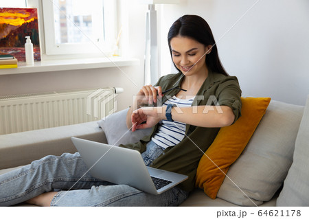 Beautiful young woman using laptop and looking at wristwatch Beautiful young woman using laptop and looking at wristwatch 64621178