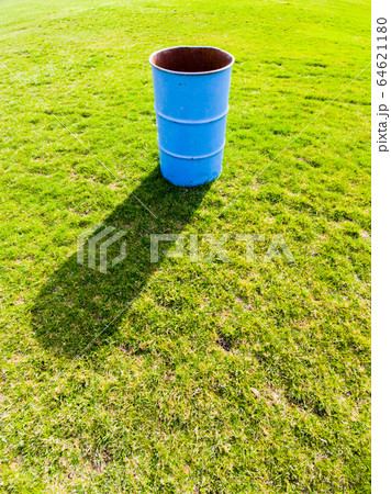 Blue garbage bin casting shadow on green grass. 64621180